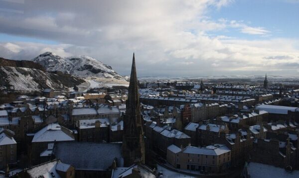 Snow-covered rooftops in Edinburgh with Arthur’s Seat in the background on a winter day.